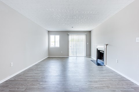 A spacious living room with a fireplace and a window with blinds.