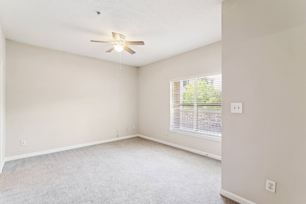 an empty living room with a large window and a ceiling fan