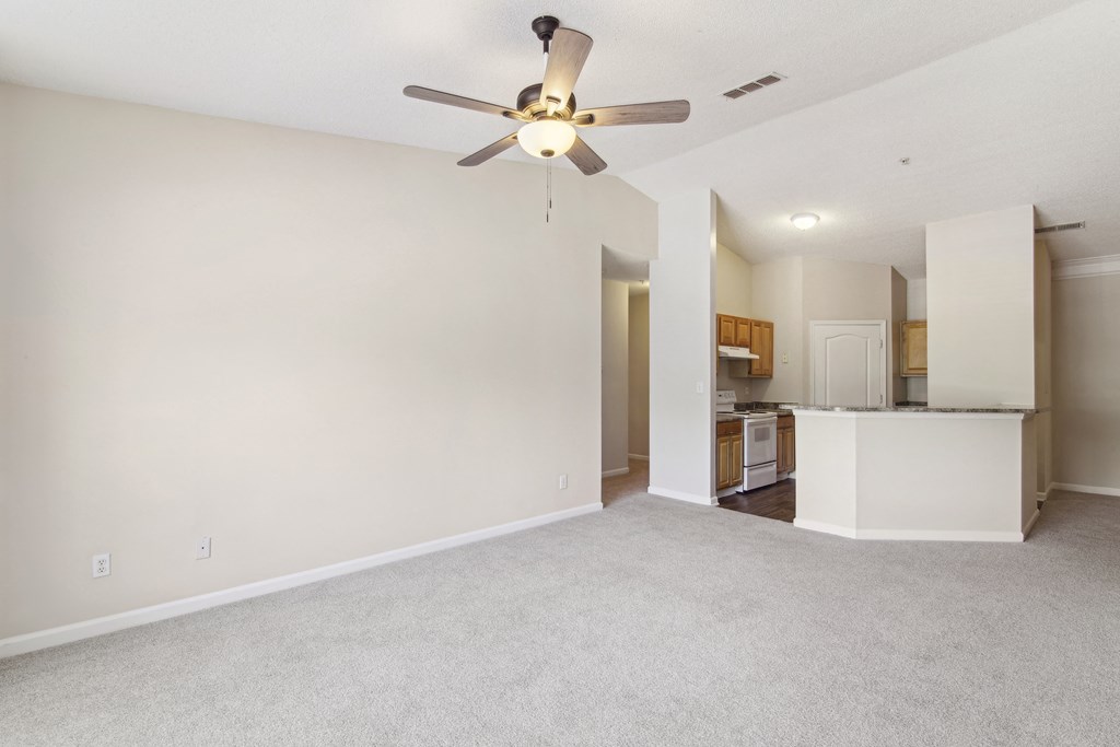 an empty living room with a ceiling fan and a kitchen