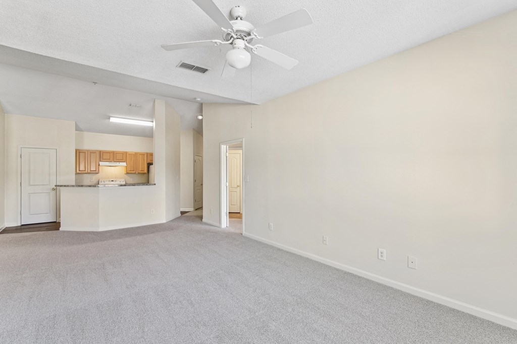 an empty living room with a ceiling fan and a kitchen