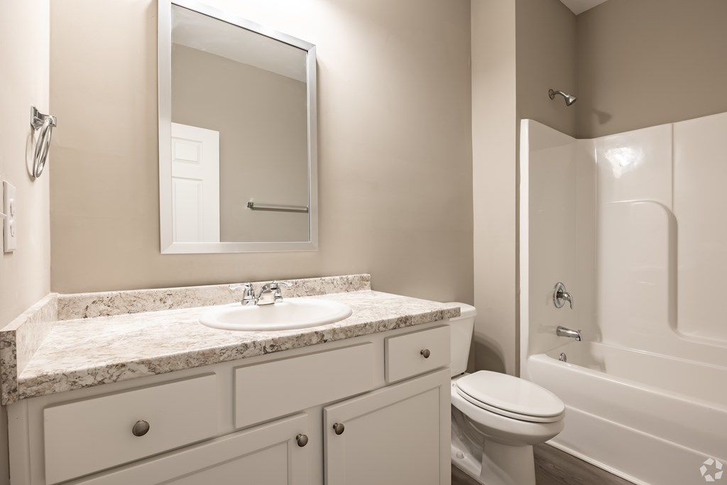 A white bathroom with a marble countertop and a white toilet at Club Villas Apartments, Kathleen, GA, 31047