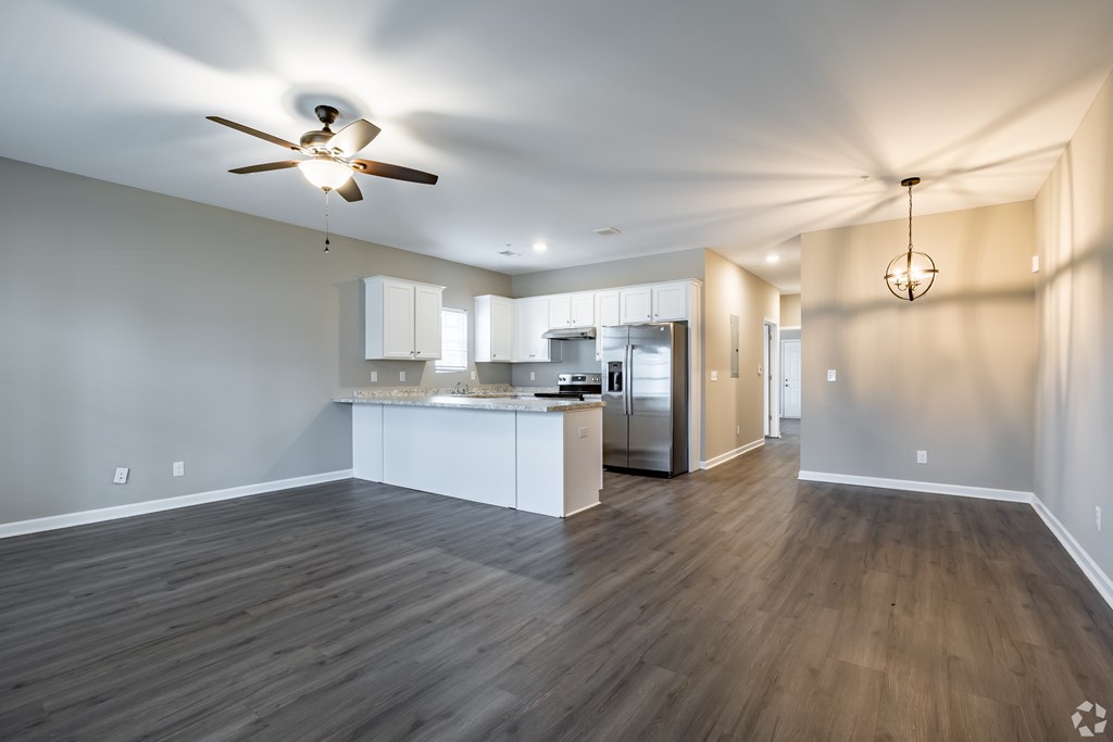 A spacious kitchen and living room with wood flooring and white walls at Club Villas Apartments, Kathleen, GA