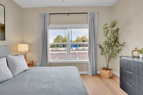 A bedroom with a large bed, a nightstand, and a window with a view of a parking lot.
