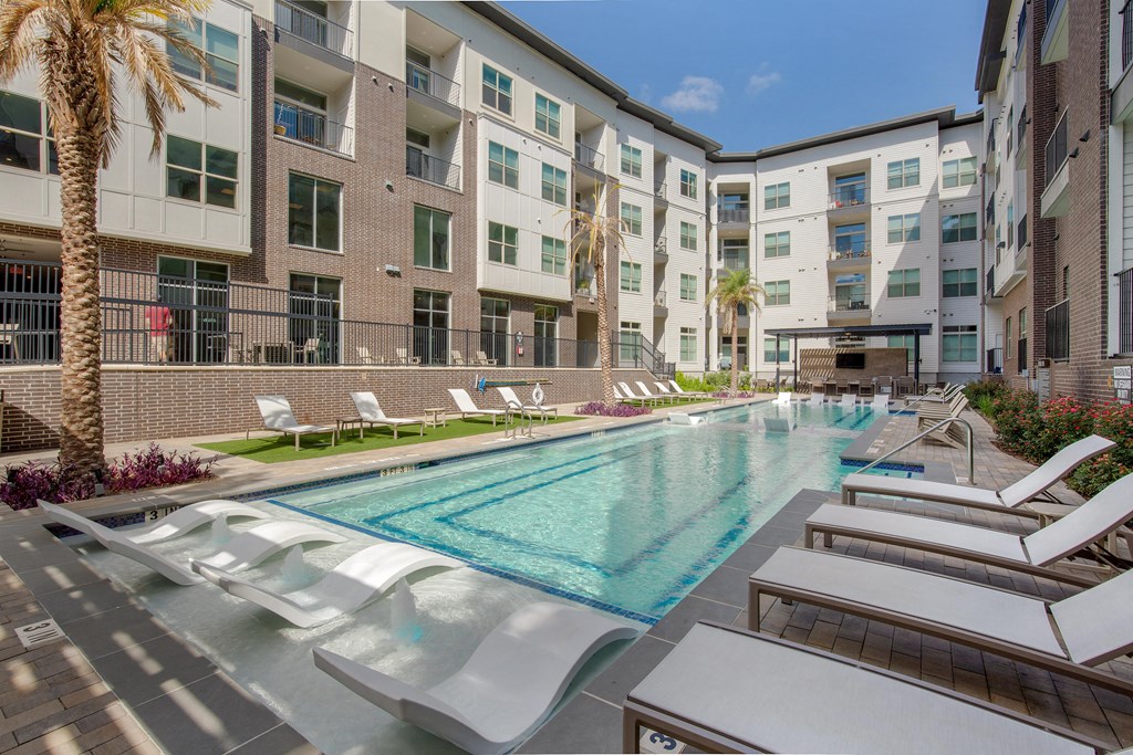 a swimming pool with lounge chairs in front of an apartment building at The Monroe Apartments, Texas, 78741