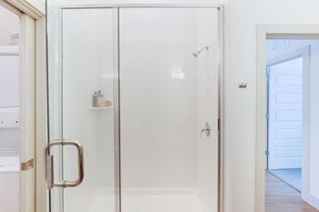 a shower with a glass door in a white bathroom at The Monroe Apartments, Texas, 78741