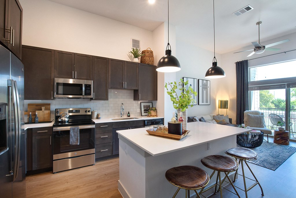a kitchen and living room with a white island and stools at The Monroe Apartments, Austin