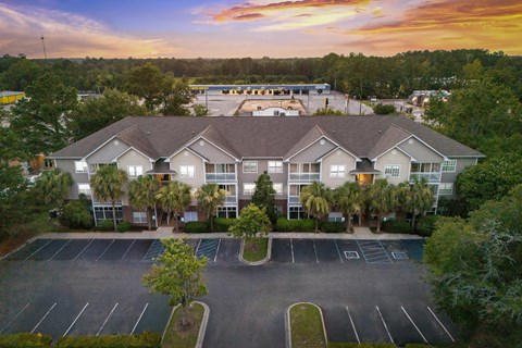 A sunset view of a large building with a parking lot in front.