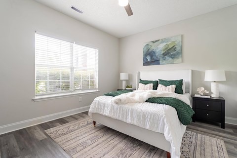 A bedroom with a large bed, two lamps, and a painting on the wall.