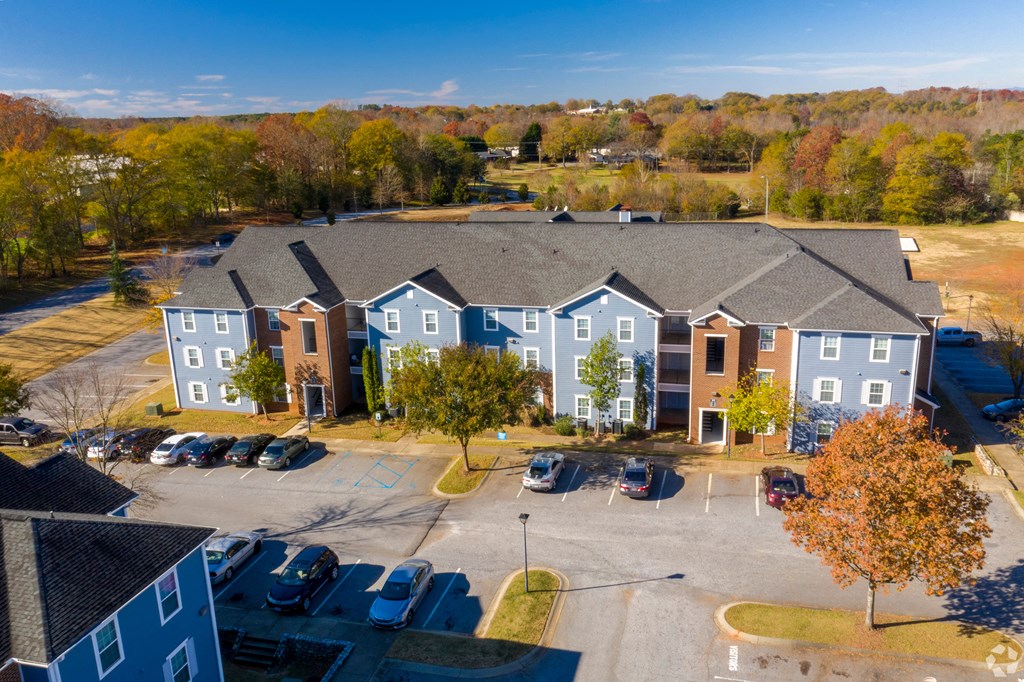 an aerial view of a large apartment complex with a parking lot and trees in the background