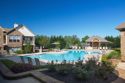 A large swimming pool surrounded by a brick patio and a small garden.