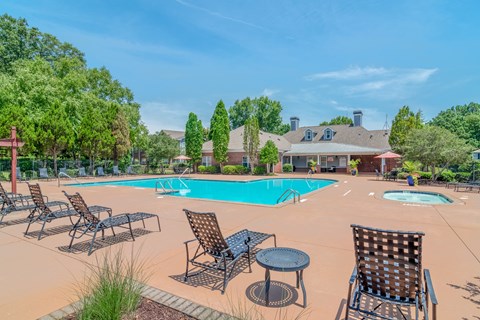 A pool surrounded by chairs and tables with a house in the background.