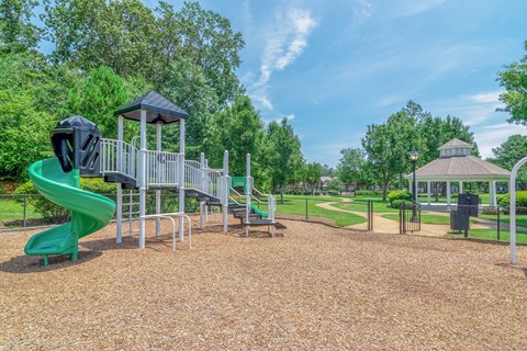 A playground with a green slide and a brown sandy area.