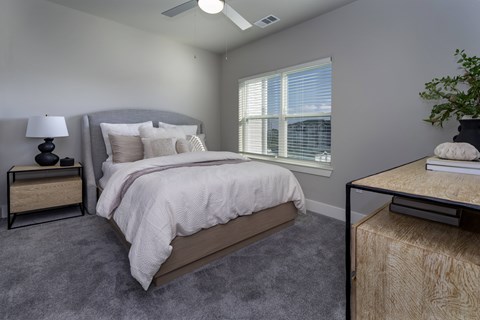 A bedroom with a large bed, a nightstand with a lamp, and a window with blinds at The Waverly at Winter Haven Apartments, Florida, 33884