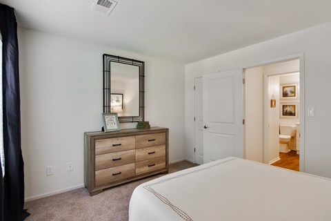 A bedroom with a large bed, a dresser with a mirror, and a door leading to another room.