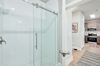 A glass shower door in a white bathroom at The Ashton at East Park Apartments, Georgia, 30144