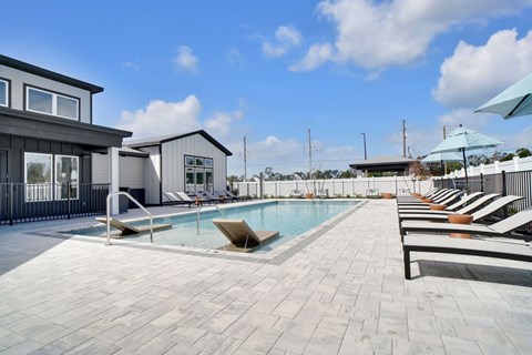A pool area with sun loungers and a building in the background.