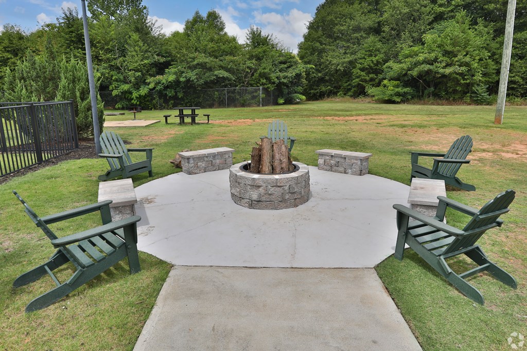 a fire pit in the middle of a grassy area with adirondack chairs