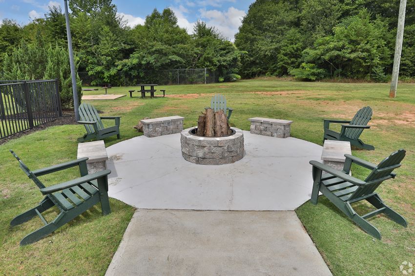 a fire pit in the middle of a grassy area with adirondack chairs - Photo Gallery