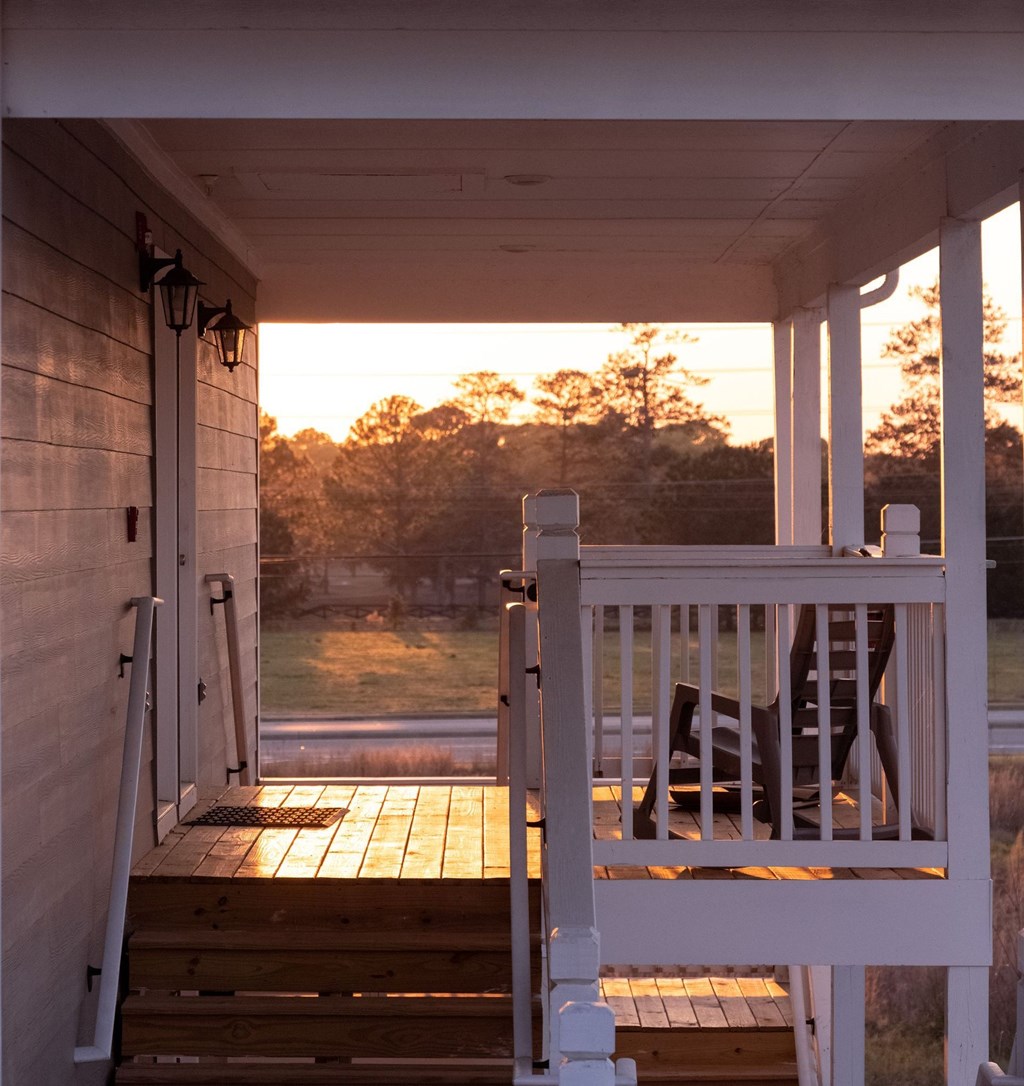 A white porch with a chair and a door leading to a grassy area at Club Villas Apartments, Kathleen, GA, 31047