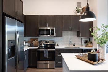 a modern kitchen with stainless steel appliances and dark cabinets at The Monroe Apartments, Austin, TX, 78741