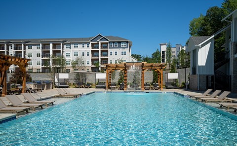 A large swimming pool with lounge chairs and a wooden pergola.