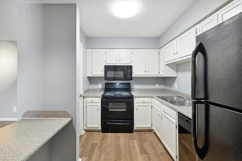 A kitchen with a black refrigerator and white cabinets.
