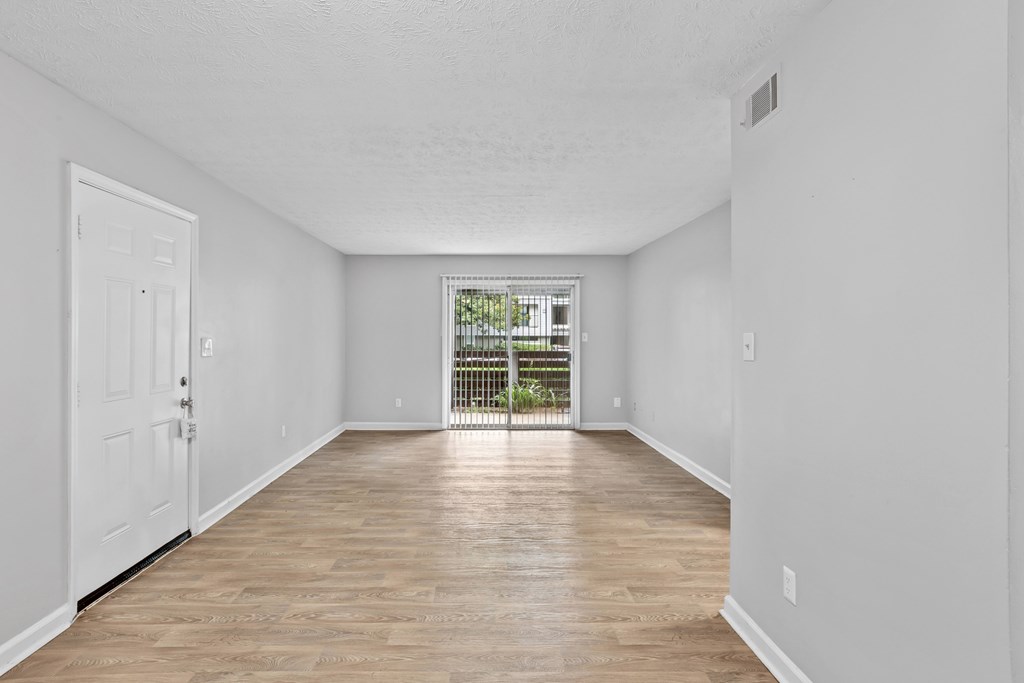A room with a white door and a window with a view of a green area.