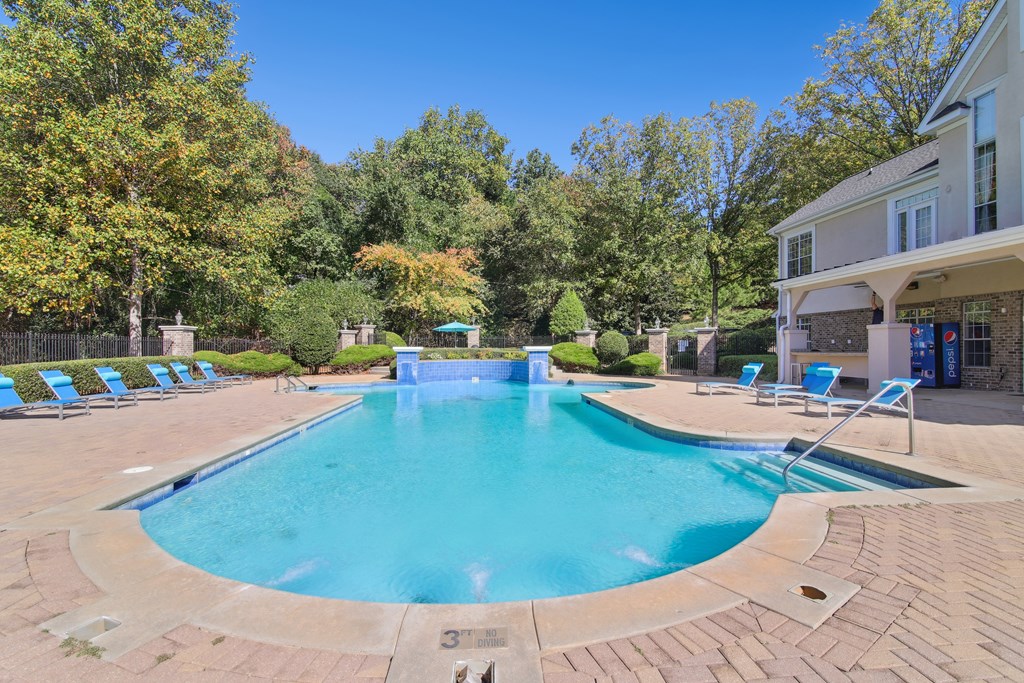 A large outdoor swimming pool surrounded by trees and lounge chairs.