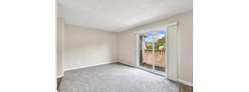 A room with a carpeted floor and a sliding glass door leading to a balcony.