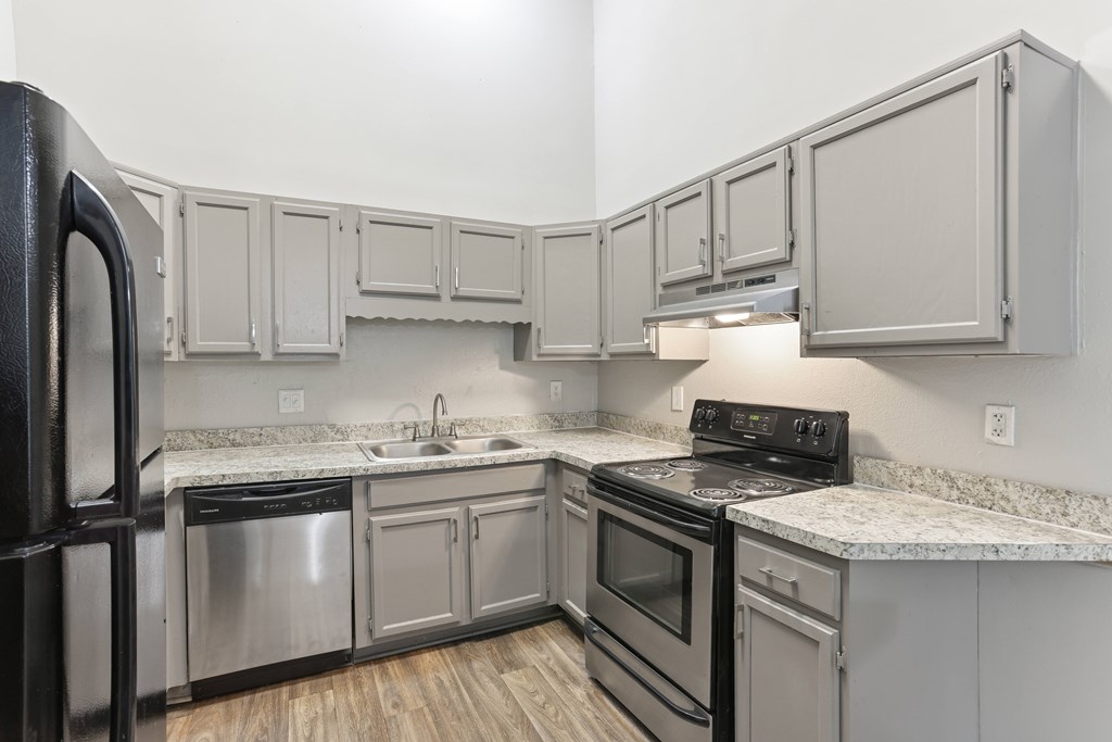 A kitchen with a black refrigerator and stove top oven.