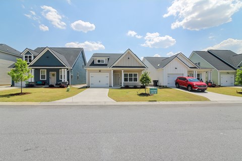A row of houses with a red car parked in the driveway of the second house from the left.