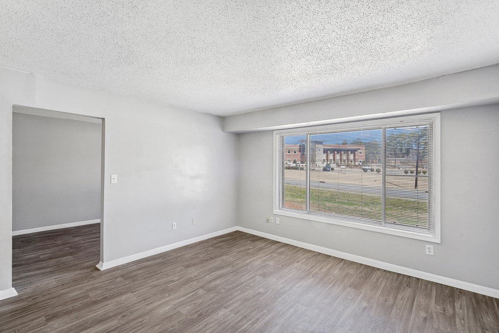the living room of an apartment with a large window and wood flooring