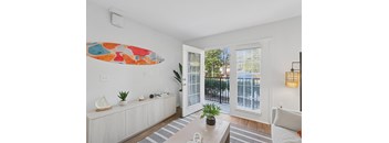 A living room with a white couch, a coffee table, and a surfboard artwork on the wall.