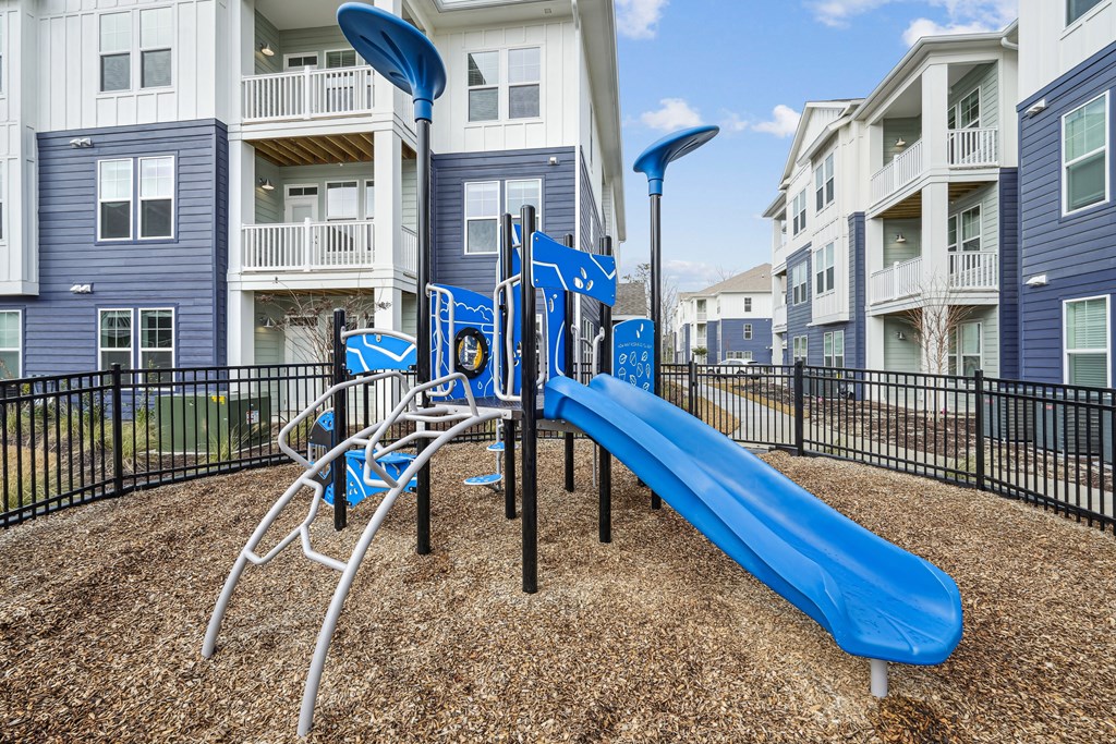A playground with a blue slide and a black fence.at The Parker Leland, Leland  