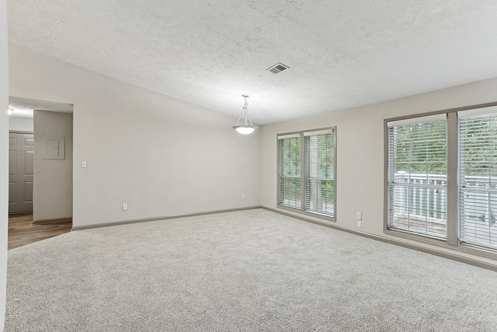 A spacious room with a carpeted floor and a window with blinds.