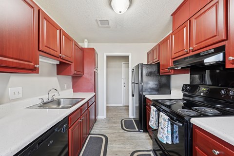 A kitchen with red cabinets and black appliances.