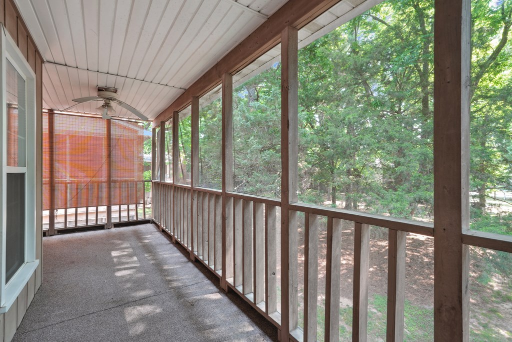 A screened-in balcony with a ceiling fan and a view of trees.