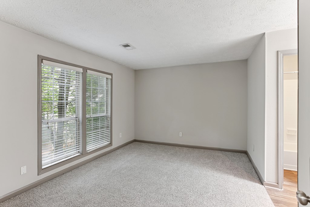 A room with a carpeted floor and a window with blinds.