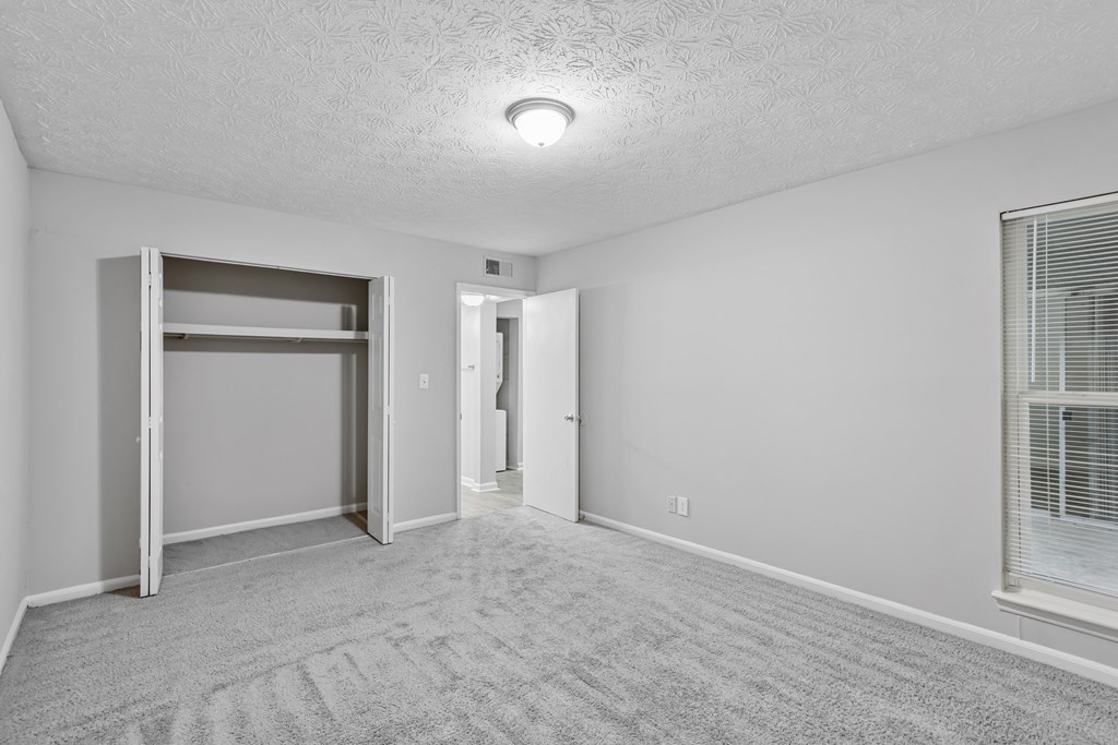 A room with a carpeted floor and a window with blinds.