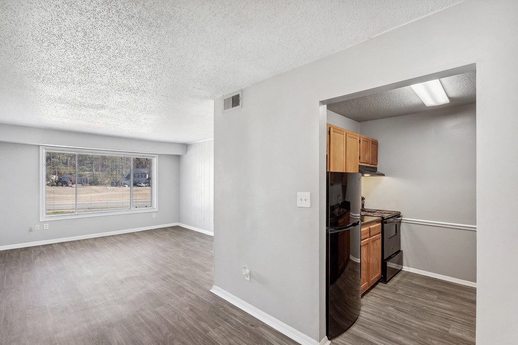 an empty living room with a kitchen and a window