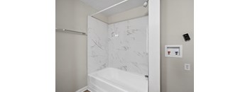 A white bathtub with a marble patterned wall behind it.