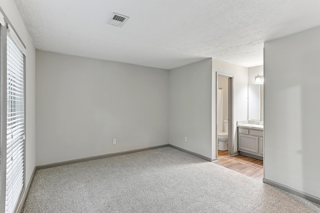 A spacious room with a carpeted floor and a window with blinds.