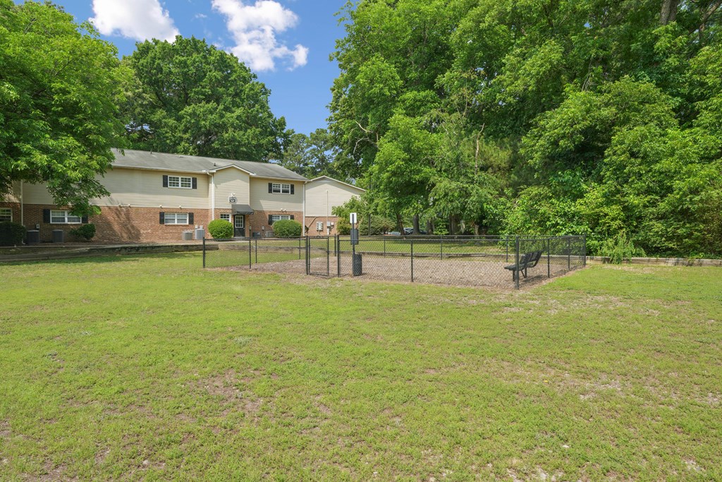 A grassy dog park with a fence and a house in the background.