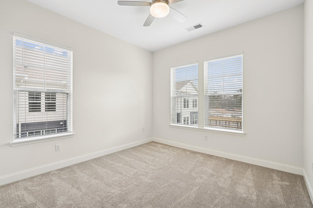 A room with a ceiling fan and two windows with blinds.at The Parker Leland, Leland, NC 28451  