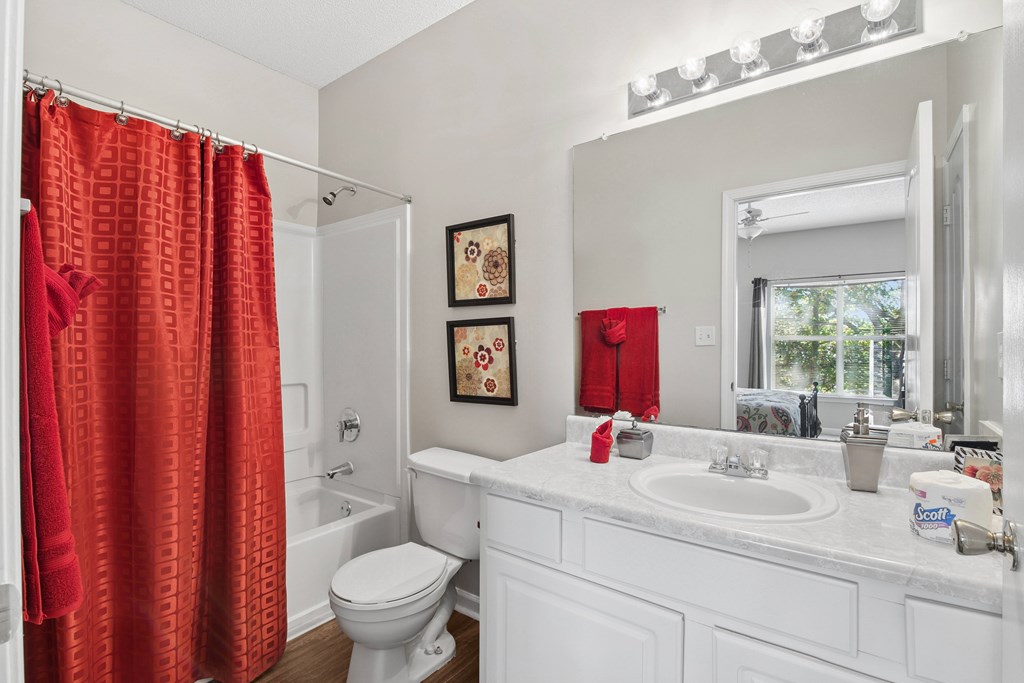 A white bathroom with a red shower curtain.