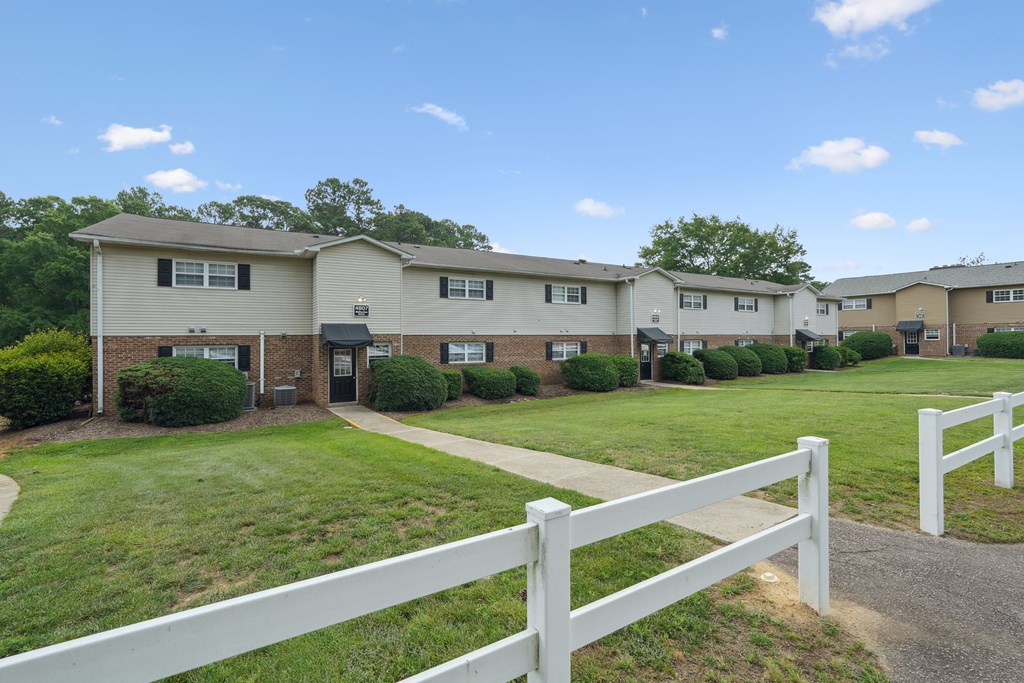 A white picket fence separates a grassy area from a row of houses.