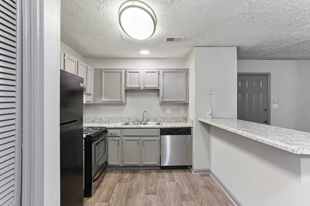 A kitchen with a black refrigerator, white cabinets, and a marble countertop.