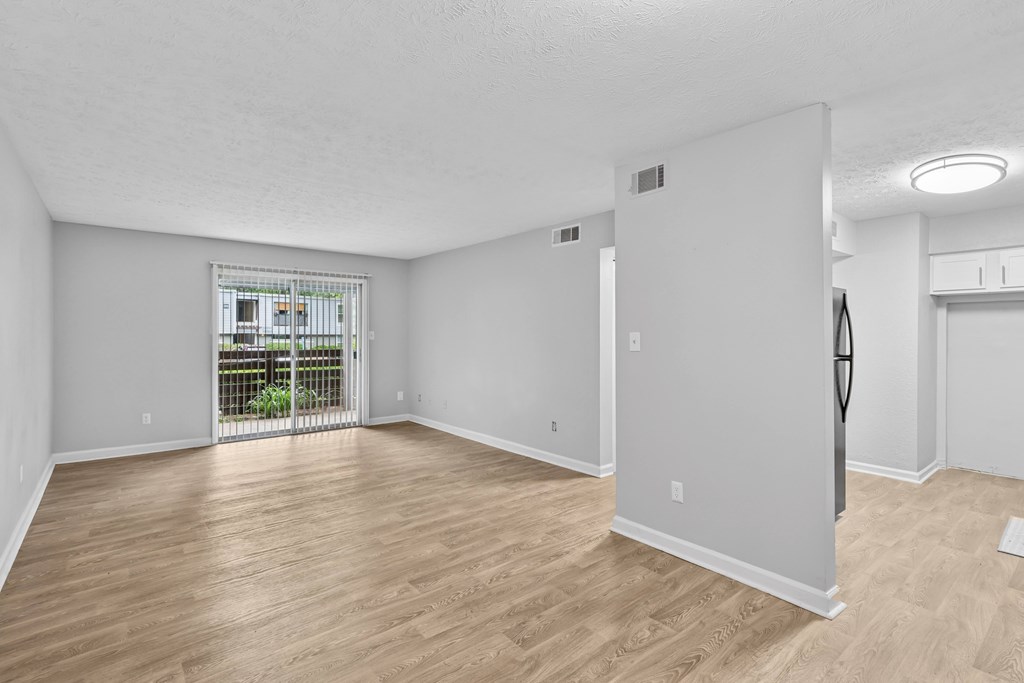 A room with wooden flooring and white walls, with a balcony visible through the door.
