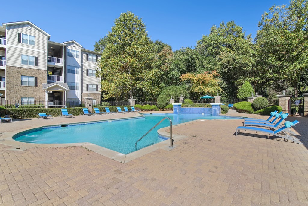 A large swimming pool surrounded by a brick patio and lounge chairs.