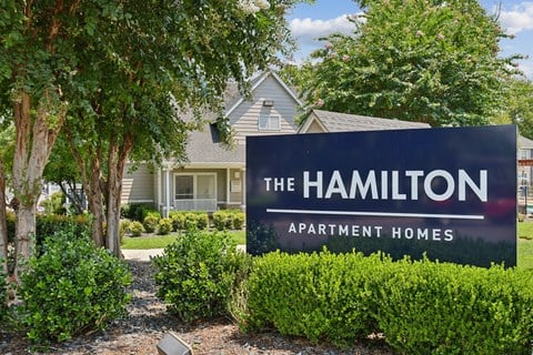 A sign for The Hamilton Apartment Homes is in front of a house.